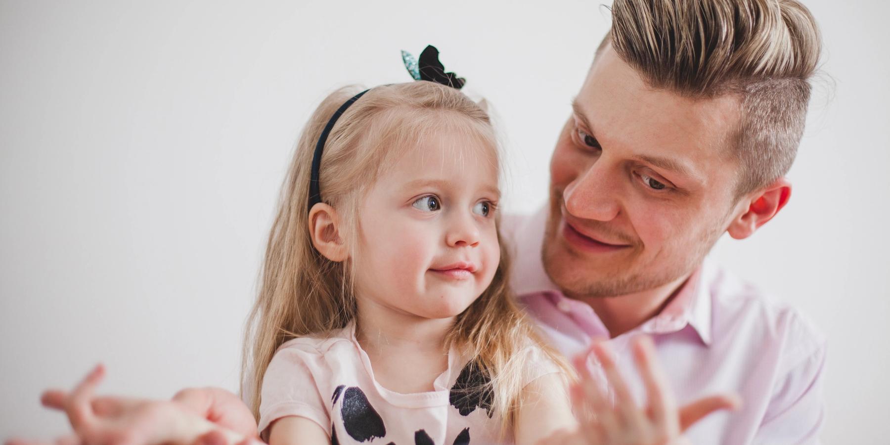Mosolygó apa játszik a lánya kezével