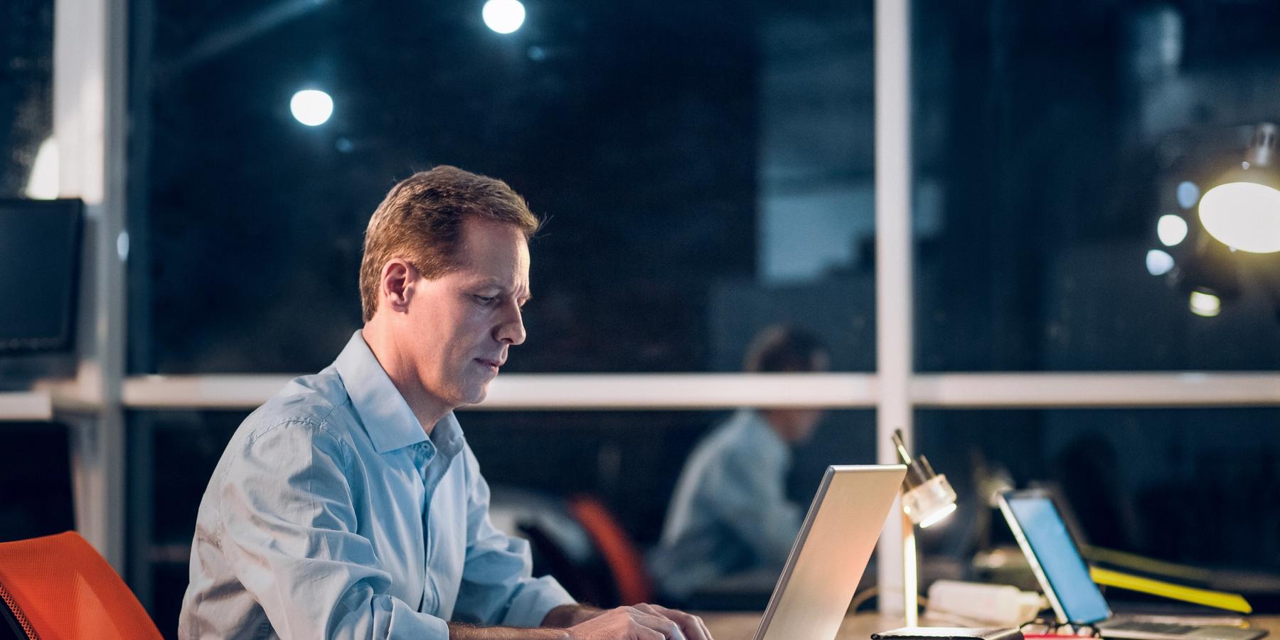 középkorú férfi asztalnál ülve dolgozik laptopon