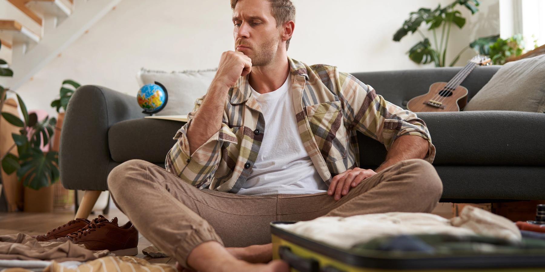 A stresszes fiatalember pakol a bőröndje, aki eldönti, milyen ruhákat hozzon a nyaralásra gondolkodva