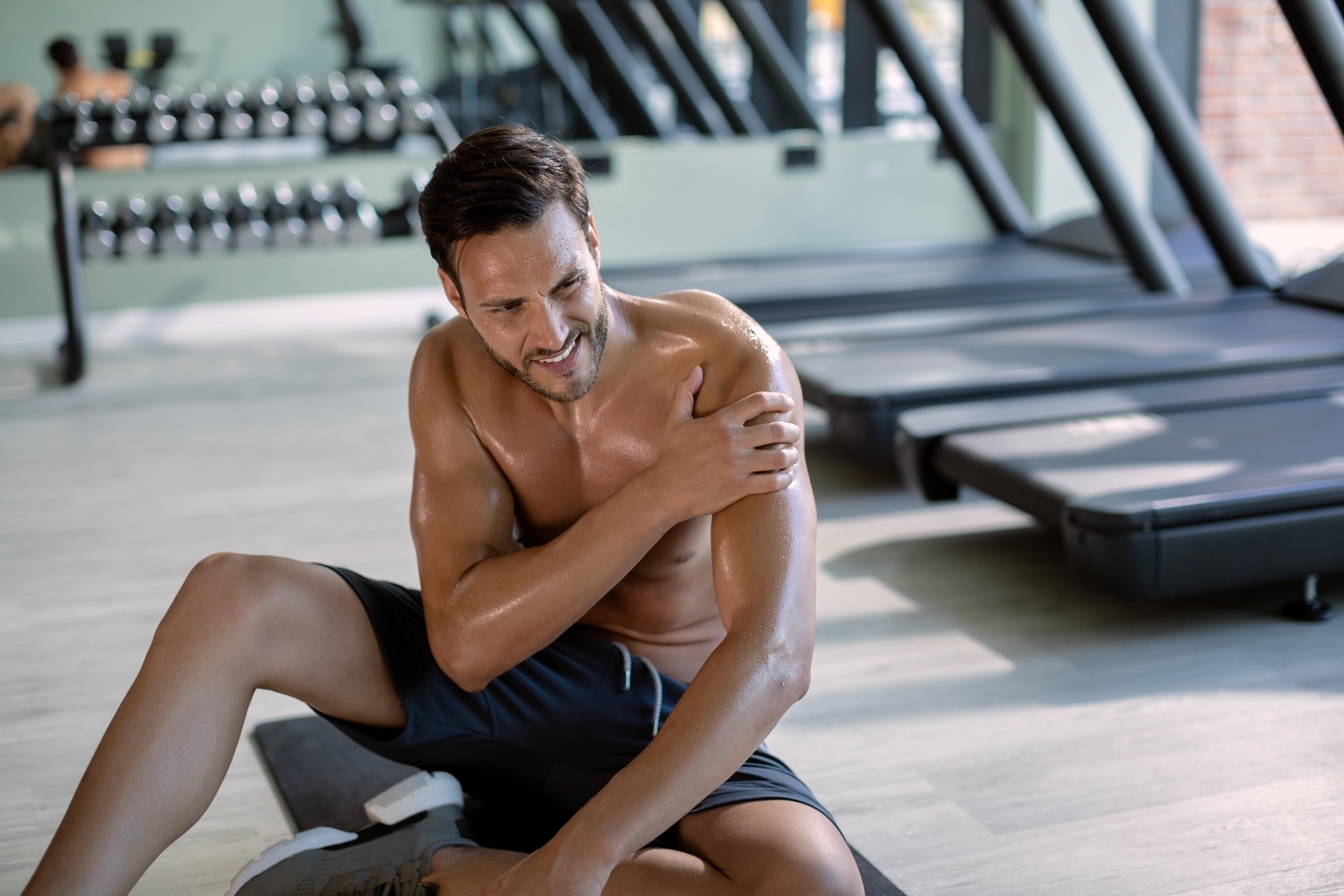 Fiatal sportoló tartja a vállát fájdalmában egy edzőteremben végzett sportedzés után