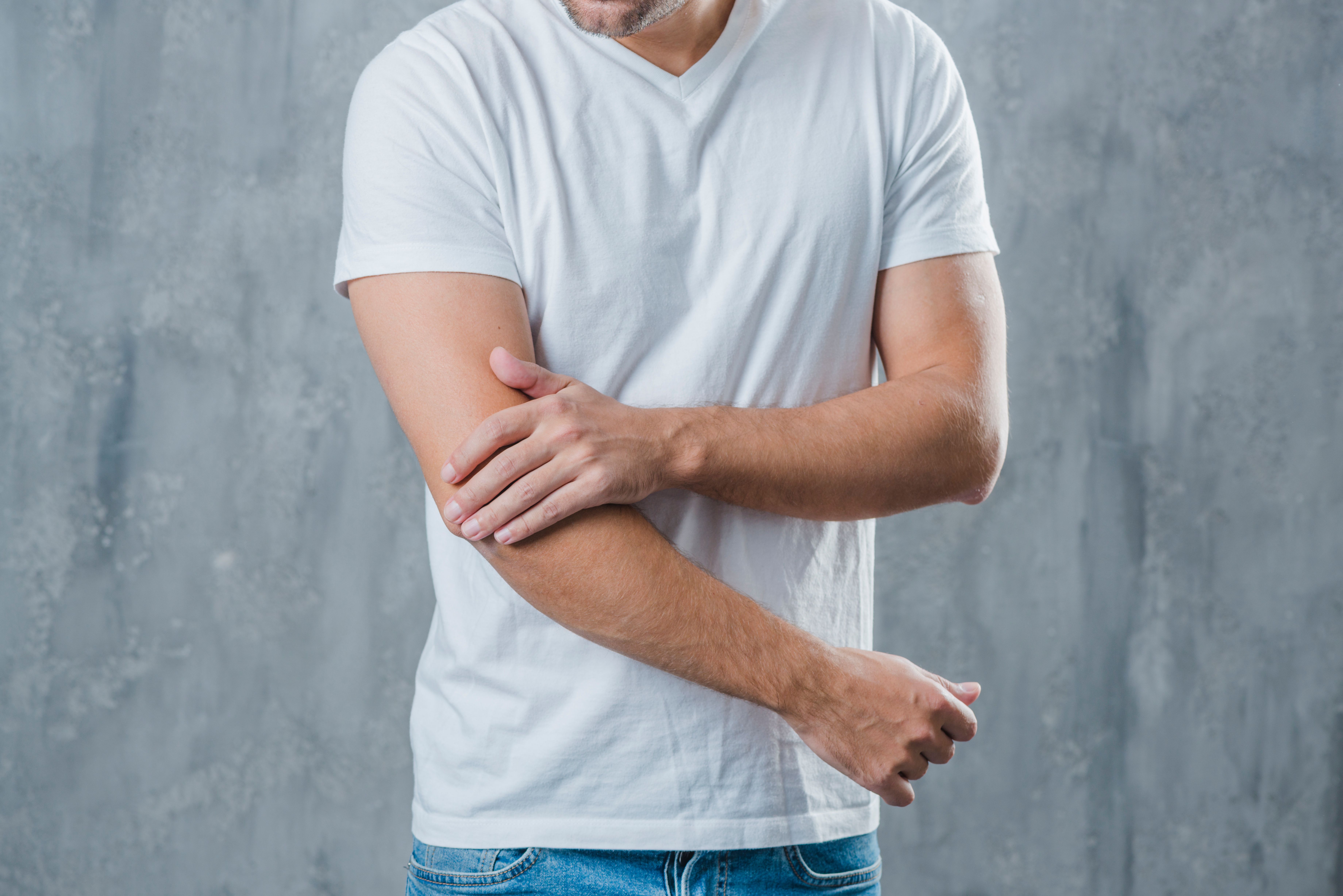 férfi fájó könyökkel, szürke háttérben