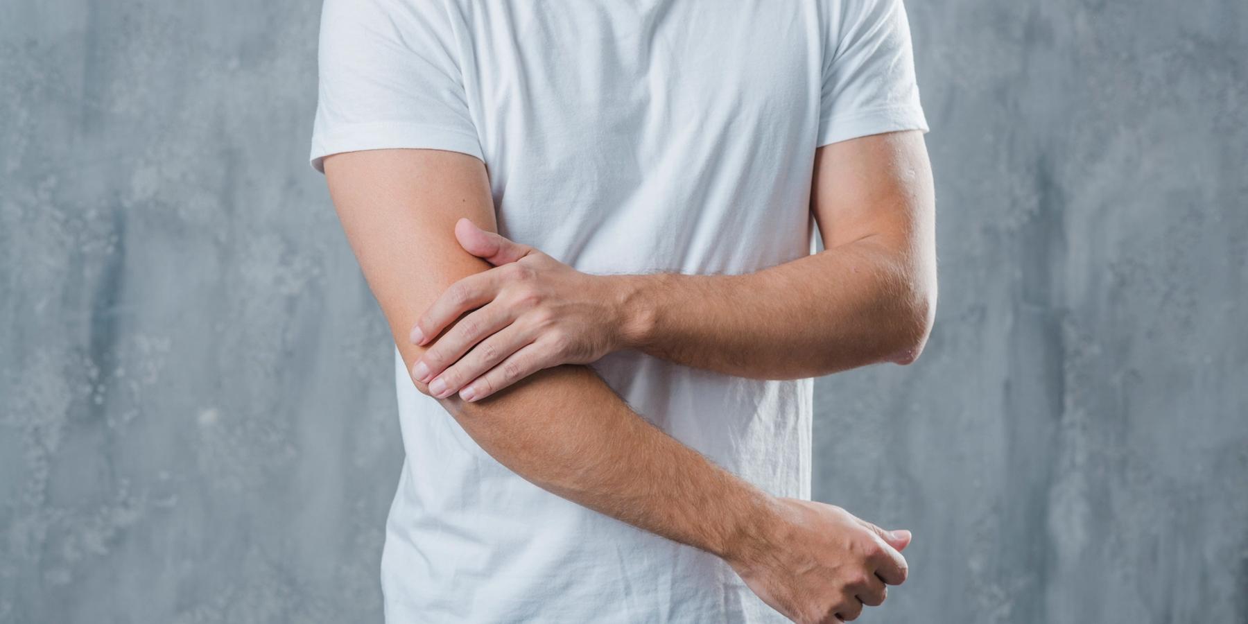 férfi fájó könyökkel, szürke háttérben