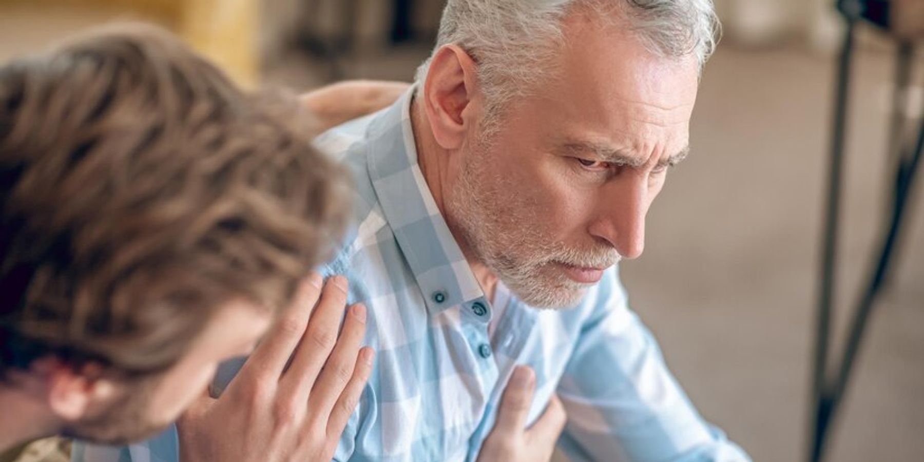 Sötét hajú férfi orvos, aki egy feldúlt, komoly, ősz hajú, mellkasi fájdalomtól szenvedő férfire néz.