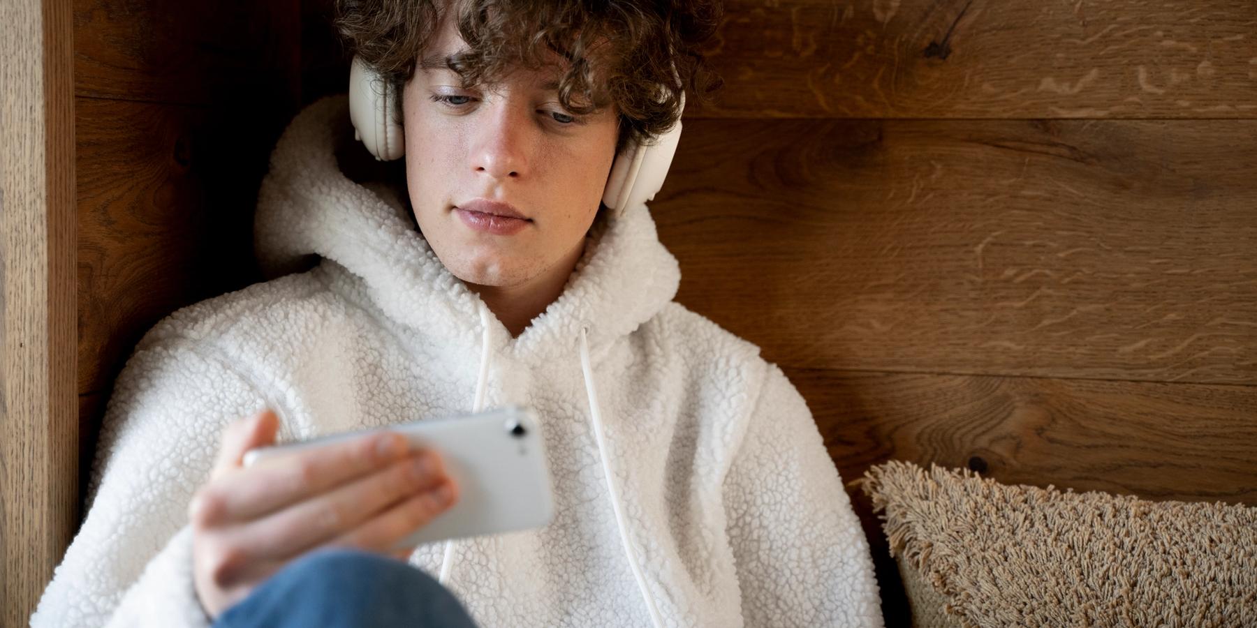 ágyon ülő kamasz fejhallgatóval zenét hallgat a telefonról