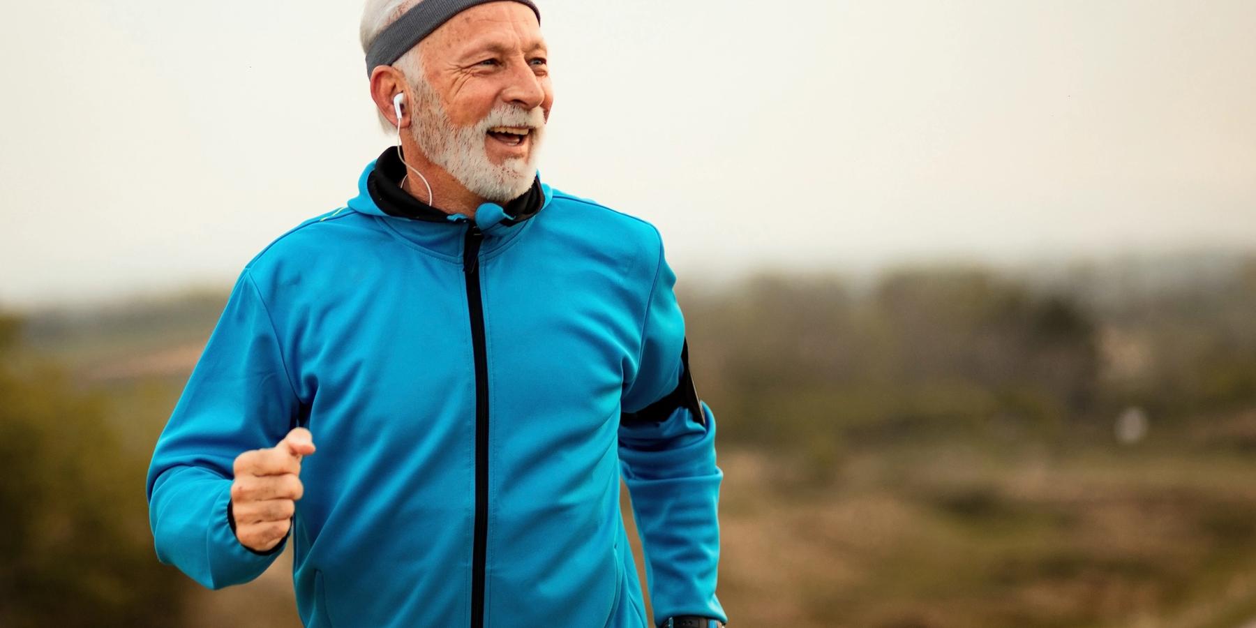 Boldog idősebb sportoló zenét hallgat fülhallgatón a természetben futás közben