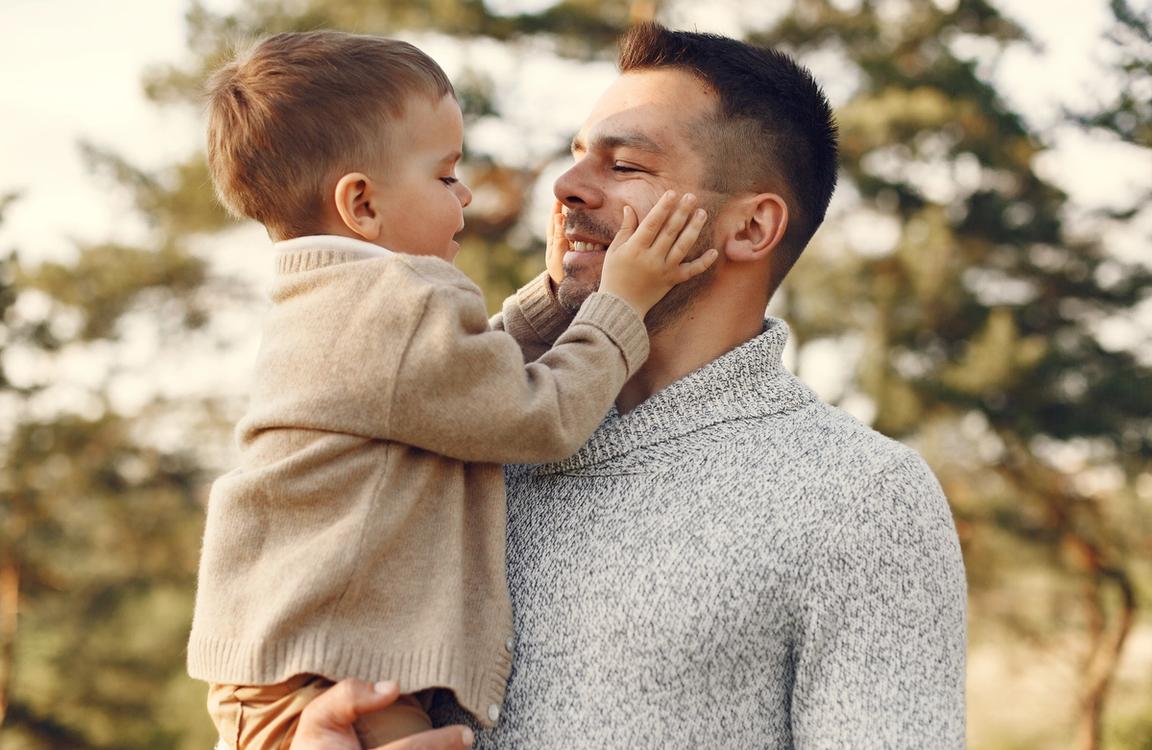 Karonülő kisfiú simogatja édesapja arcát egy erdő előtt állva