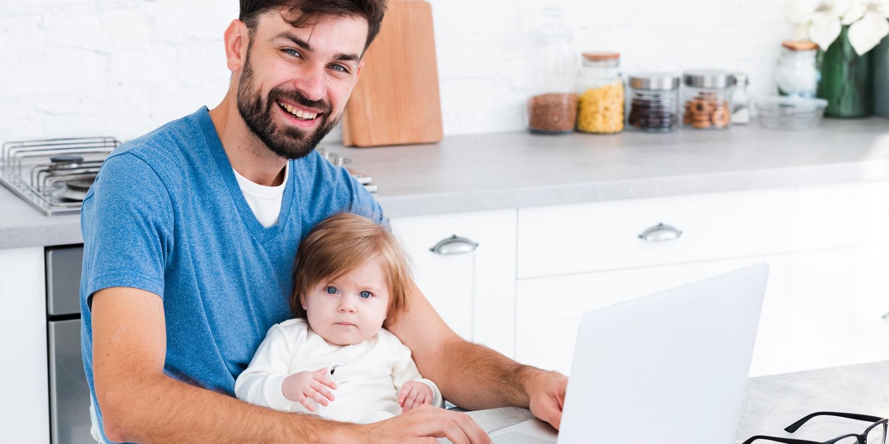 mosolygó apa laptopon dolgozik gyerekkel az ölében