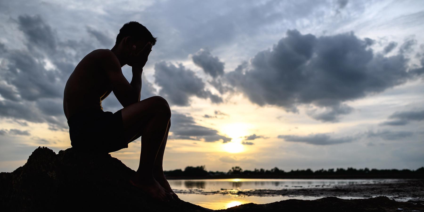 Egy férfi egy fa tövében ül behajlított a térdekkel, kezében az arcával, amint víz veszi őt körül.