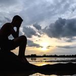 Egy férfi egy fa tövében ül behajlított a térdekkel, kezében az arcával, amint víz veszi őt körül.