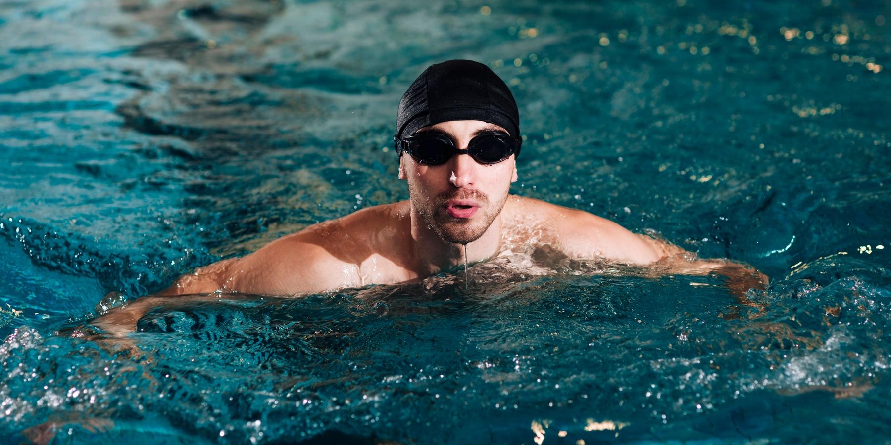 Úszósapkás, úszószemüveges férfi a medencében