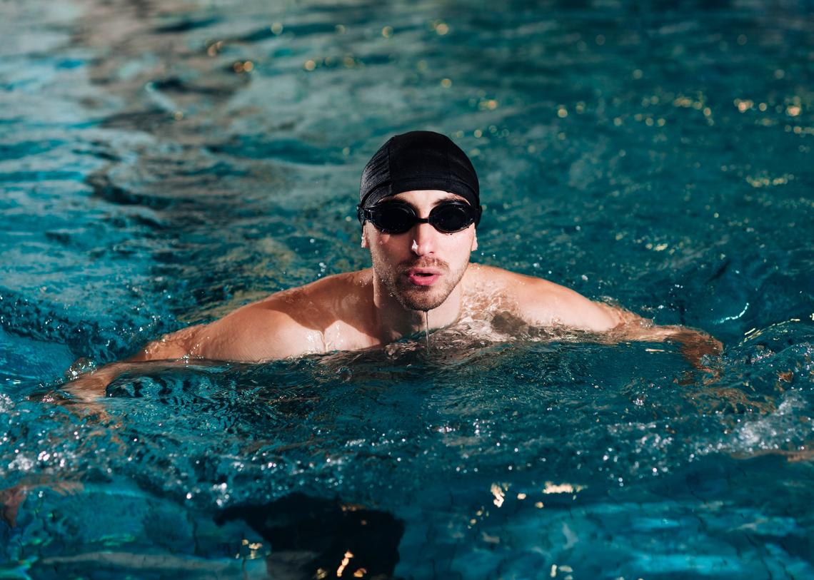 Úszósapkás, úszószemüveges férfi a medencében