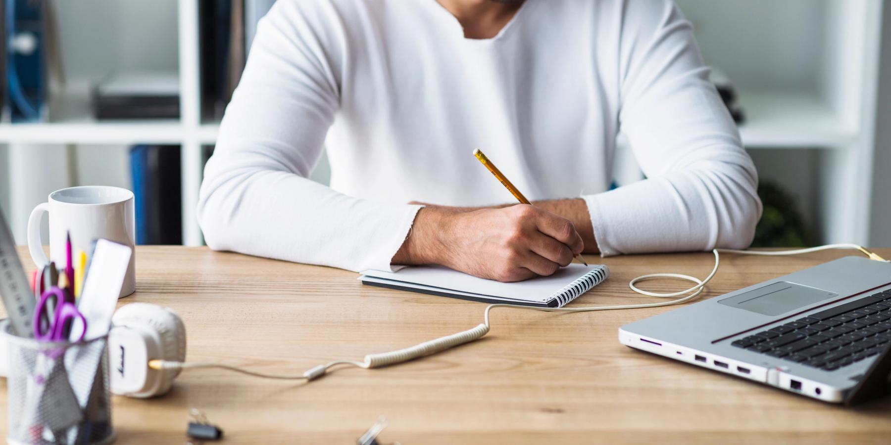 Üzletember jegyzetel egy jegyzettömbbe, fa íróasztalnál.