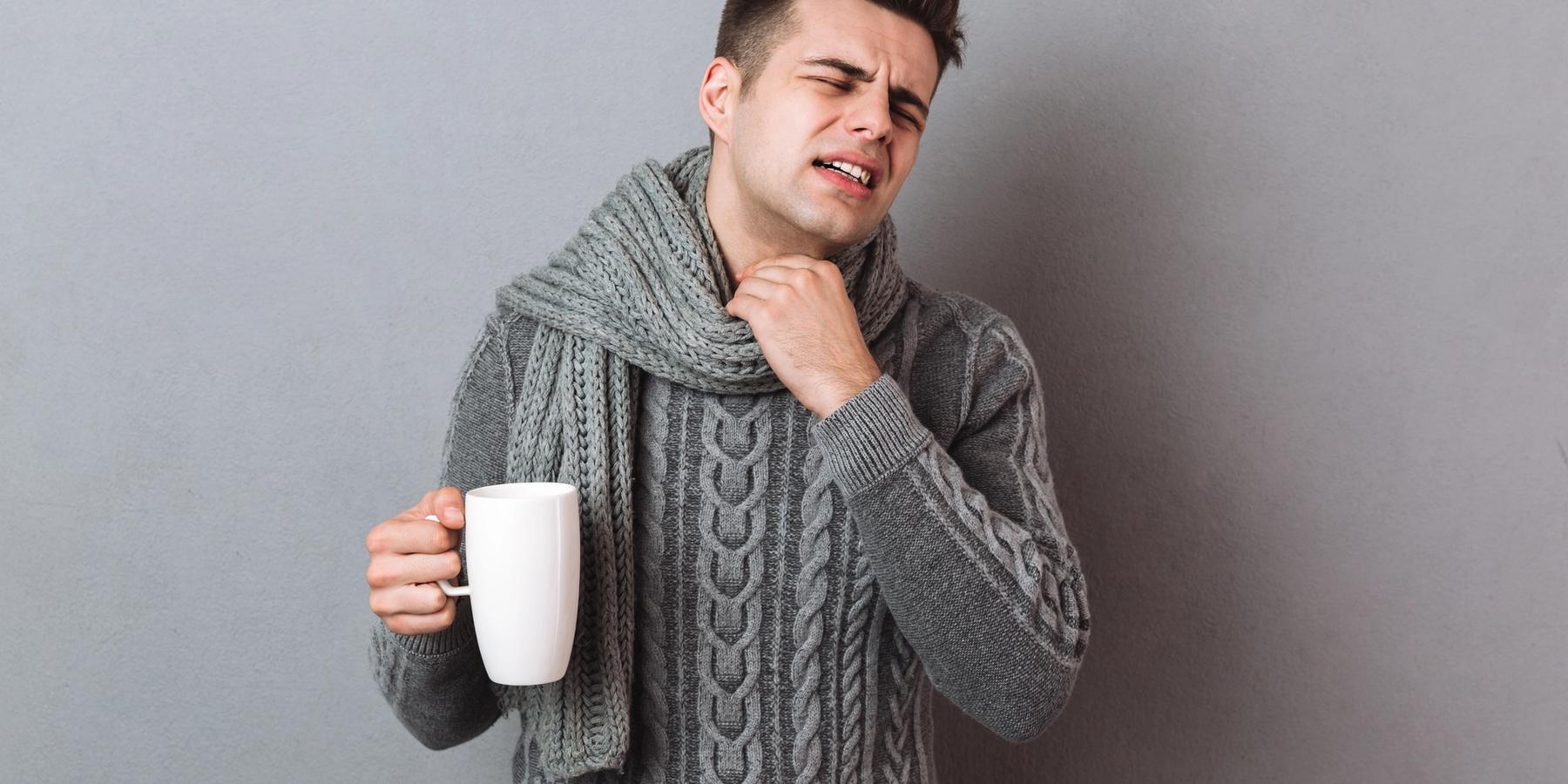 Rosszkedvű, beteg férfi, aki meleg sálat visel és forró teát tart a kezében.