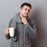 Rosszkedvű, beteg férfi, aki meleg sálat visel és forró teát tart a kezében.