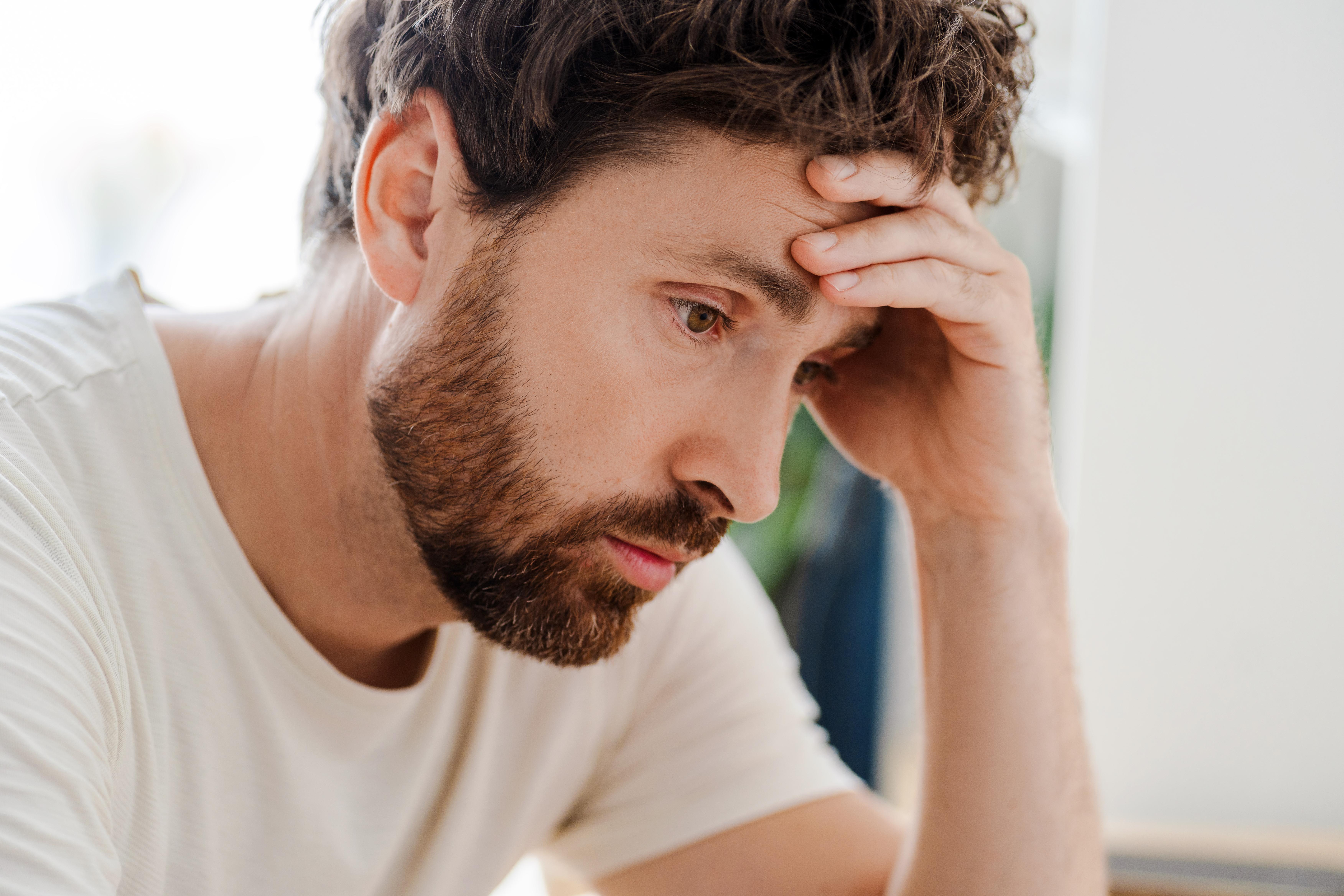 elgondolkodó fiatal férfi otthon ülve, közelkép