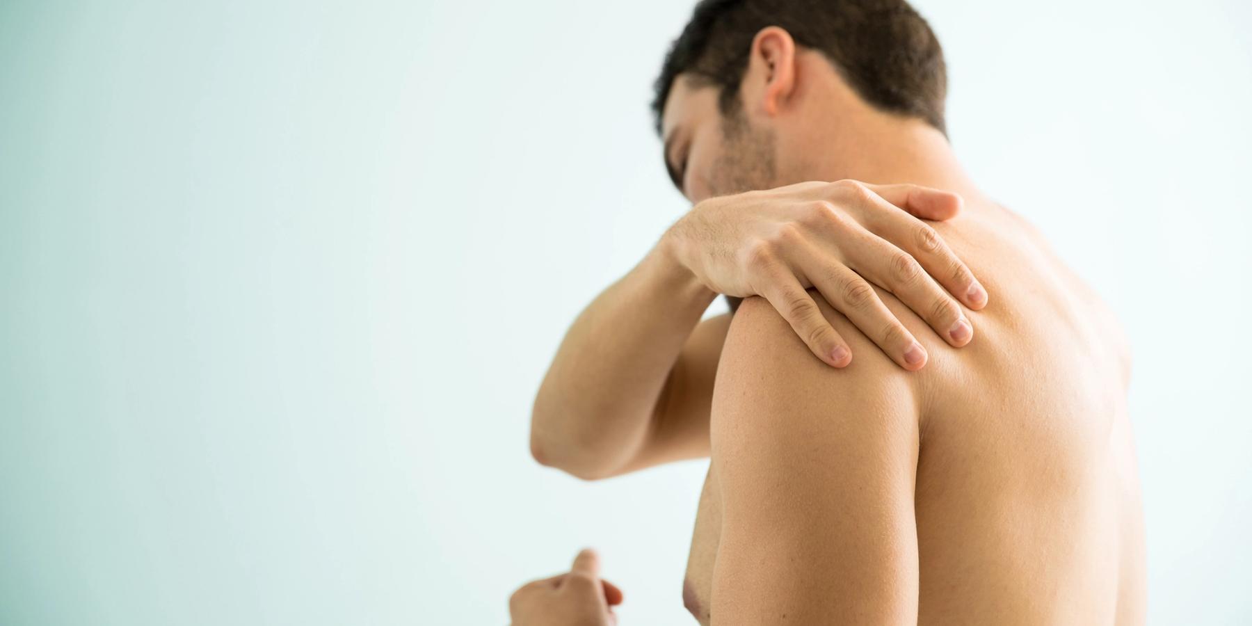 Póló nélküli fiatalember, aki izomfájdalomtól szenved a vállán