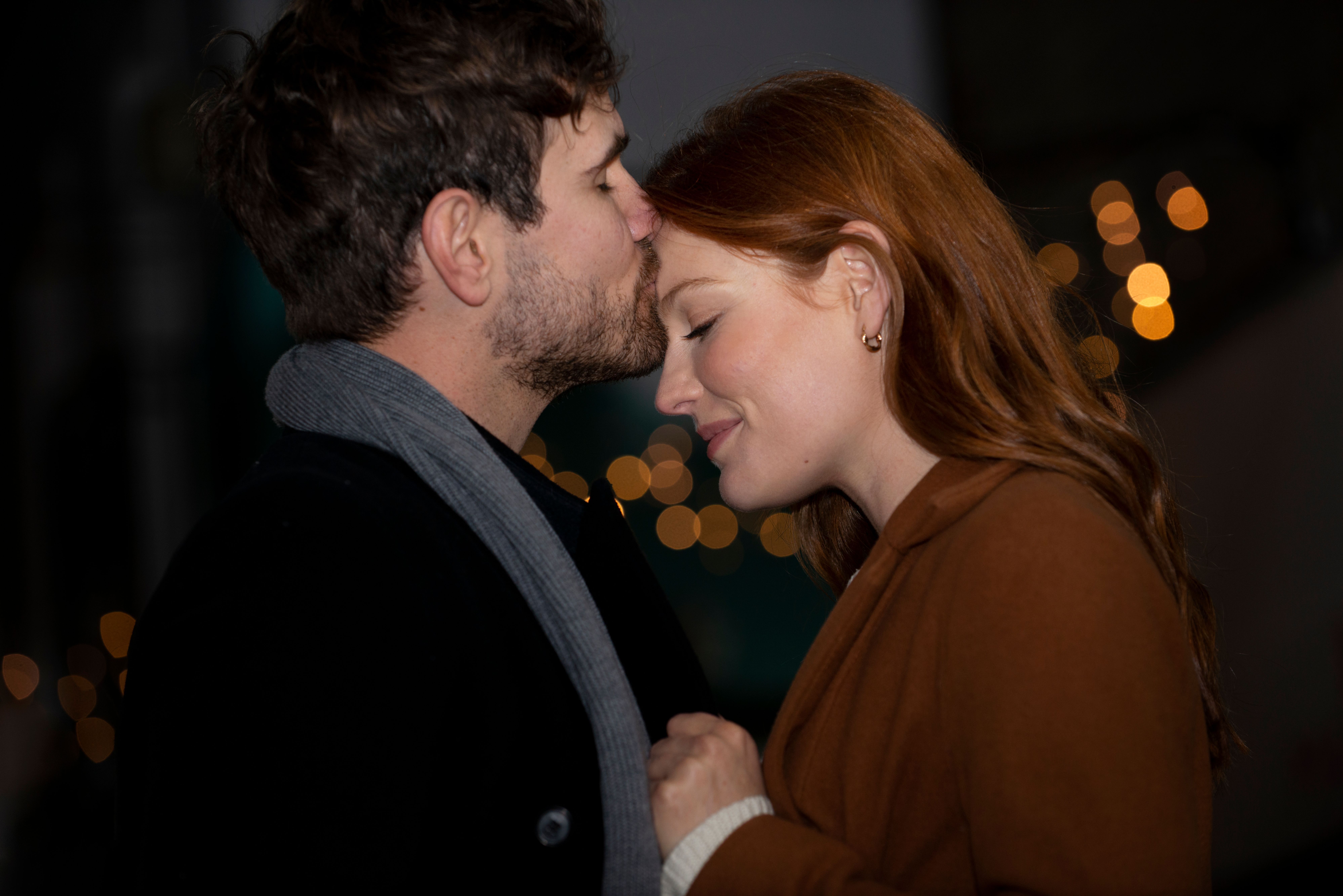 Barátnője homlokát pusziló férfi, éjszakai utcakép a háttérben