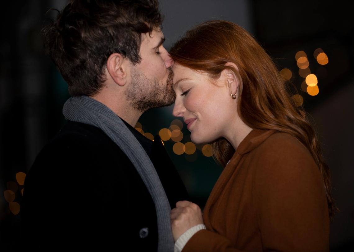 Barátnője homlokát pusziló férfi, éjszakai utcakép a háttérben