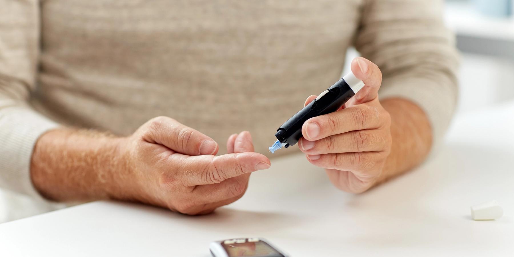 közeli kép egy idősebb férfiról, aki vérvizsgálatot végez és ellenőrzi a vércukorszintet otthonában
