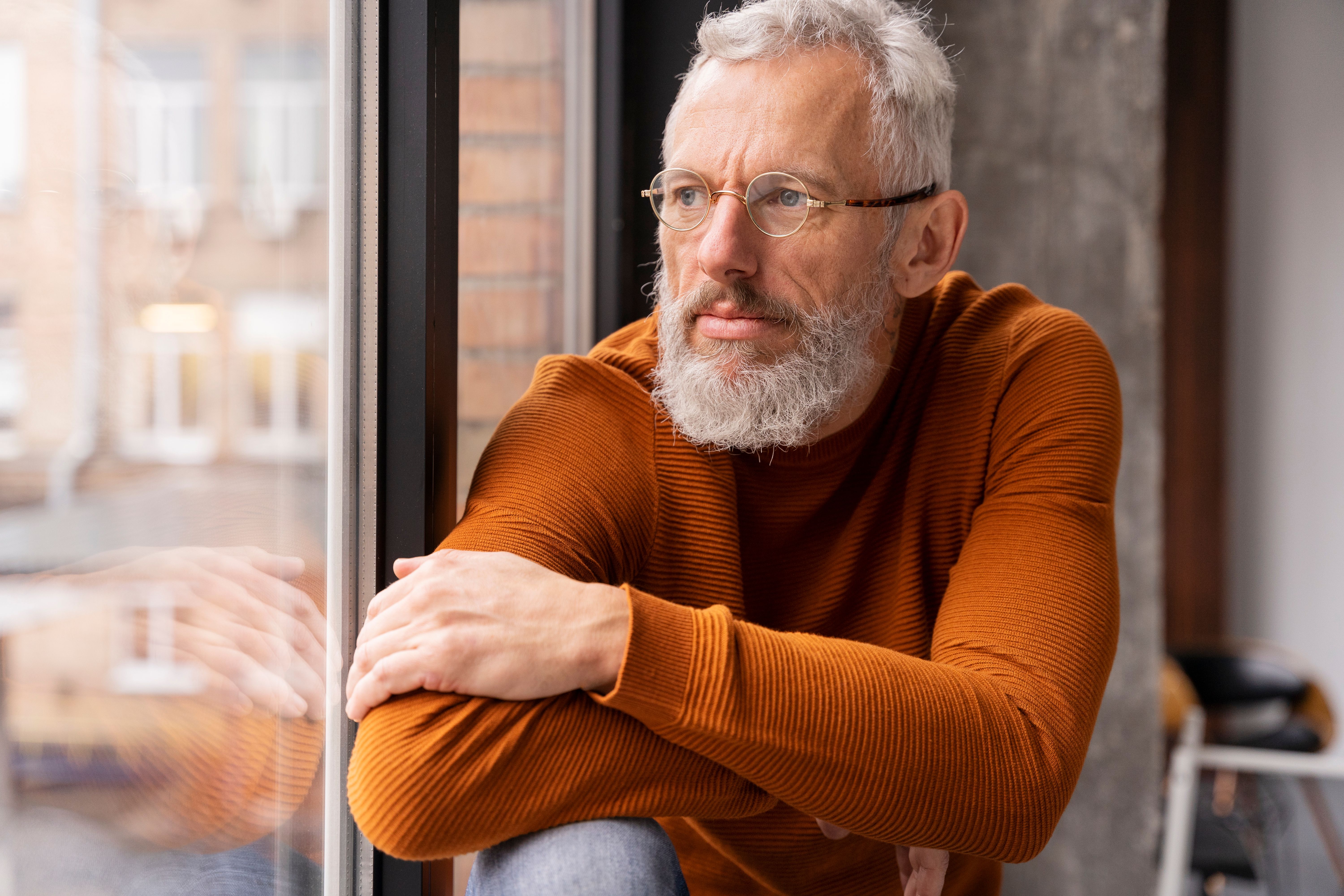 Közeli portré egy ablakon kinéző idősebb férfiról