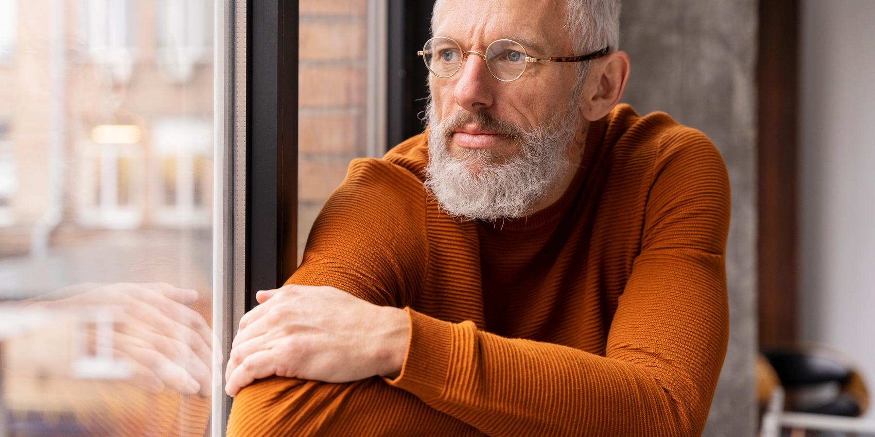 Közeli portré egy ablakon kinéző idősebb férfiról