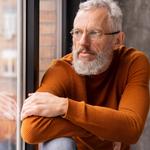 Közeli portré egy ablakon kinéző idősebb férfiról