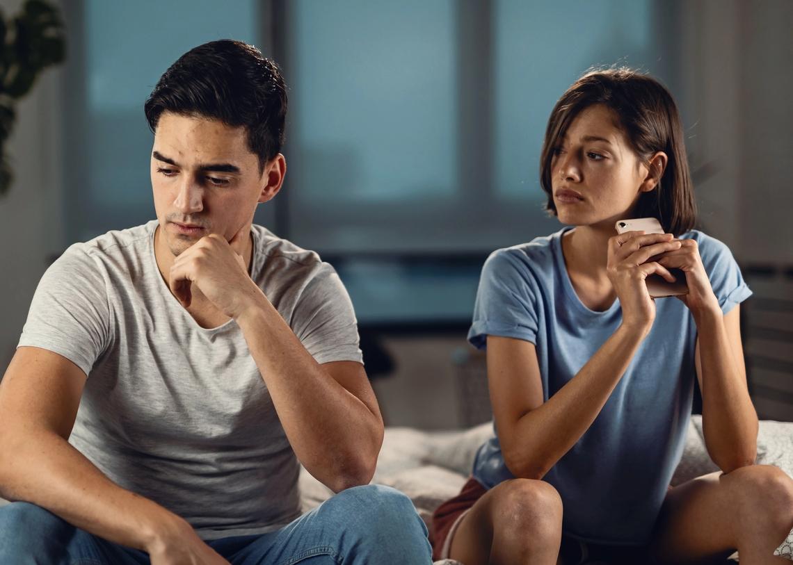 Fiatal aggódó férfi gondolkodik valamin, miközben barátnője mellett ül, és kapcsolati problémái vannak vele