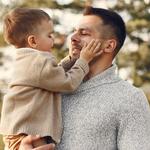 Karonülő kisfiú simogatja édesapja arcát egy erdő előtt állva