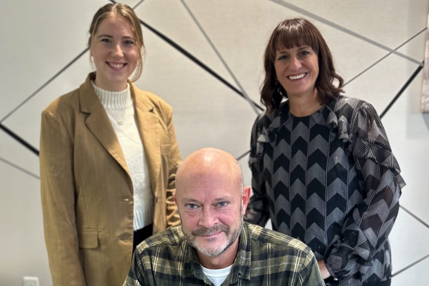 Courtney, Joe, and Julie standing in front of wall with patterned wallpaper