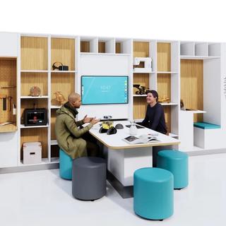 Two people sitting in an open workspace a wall of open cabinets