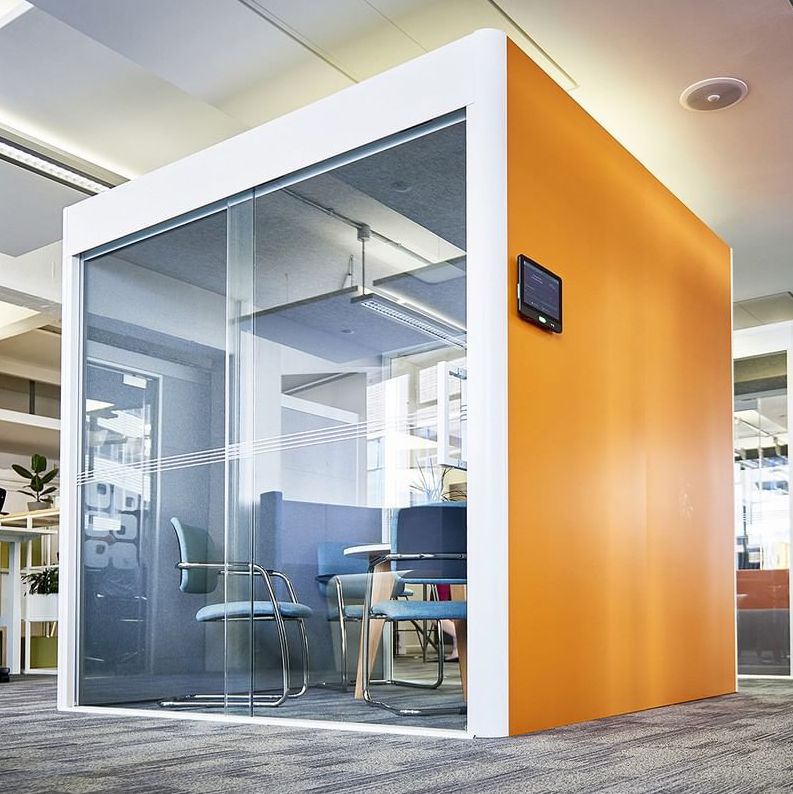 Blue office pod with white hightop table that has brown legs and a chair