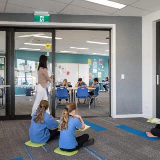 Children sitting down on green pads in room with acoustic wallcovering