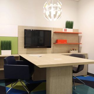 Three H desk that is light wood with a green plant, a mounted black monitor, and two chairs