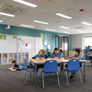 Children in schoolroom setting around table with blue chairs with acoustic wallcovering