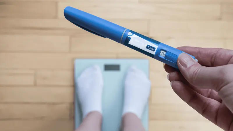 Person holding medication pen over scale - Microdosing GLP 1