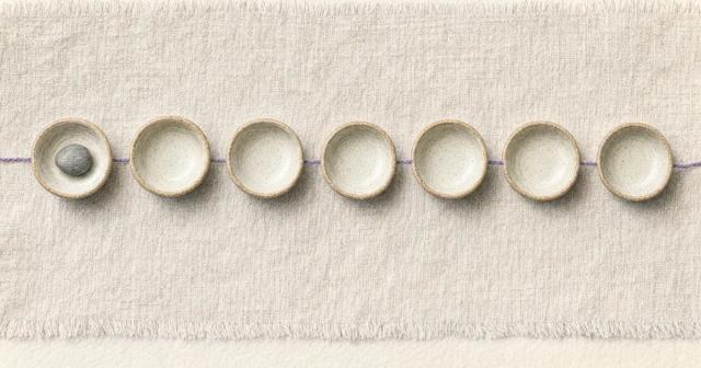 Seven small ceramic dishes in a row, only the first one holding a single pebble