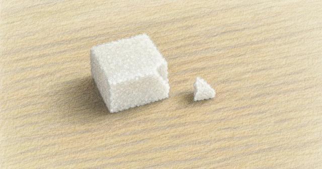 A sugar cube on a wooden table with one broken-off corner resting beside it
