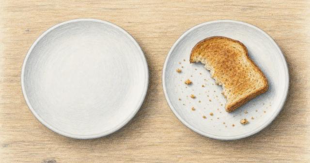Two identical plates on a wooden table, one empty and one holding a half-eaten slice of toast