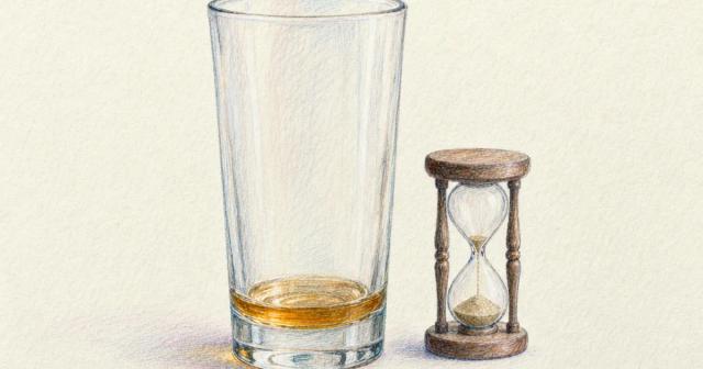 A nearly empty glass of amber liquid beside an hourglass with most of its sand fallen