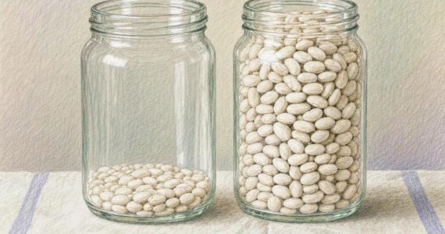 Two matching glass jars side by side, one barely covered with beans, one nearly full