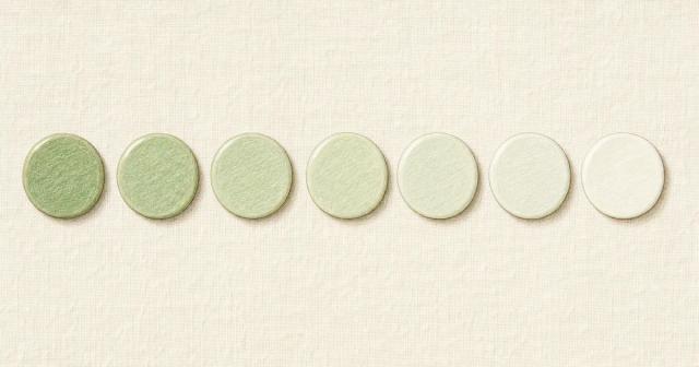 Row of seven ceramic tiles fading from sage green to near white on pale linen