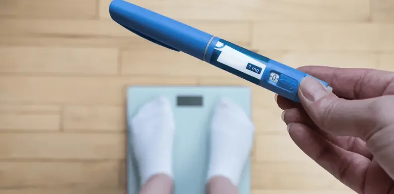 Person holding pen over scale - Who Should Not Take Semaglutide