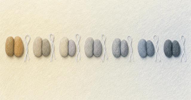 Seven evenly spaced pairs of small stones in a row on pale wood, light shifting warm to cool