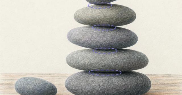 A balanced stack of smooth river stones on a wooden table with one spare stone beside it