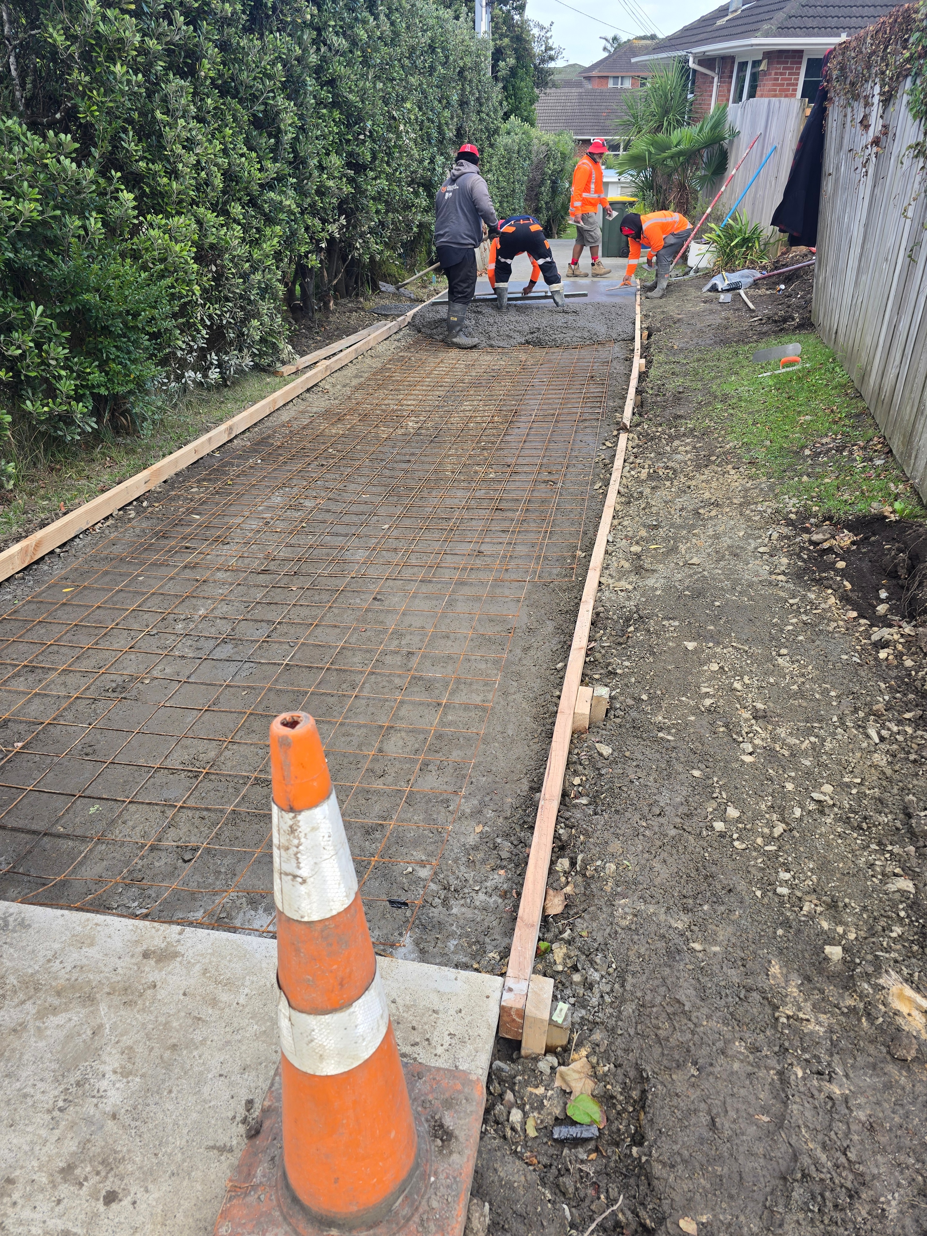 Four crew in hi-vis screeding wet concrete over steel mesh in a boxed driveway