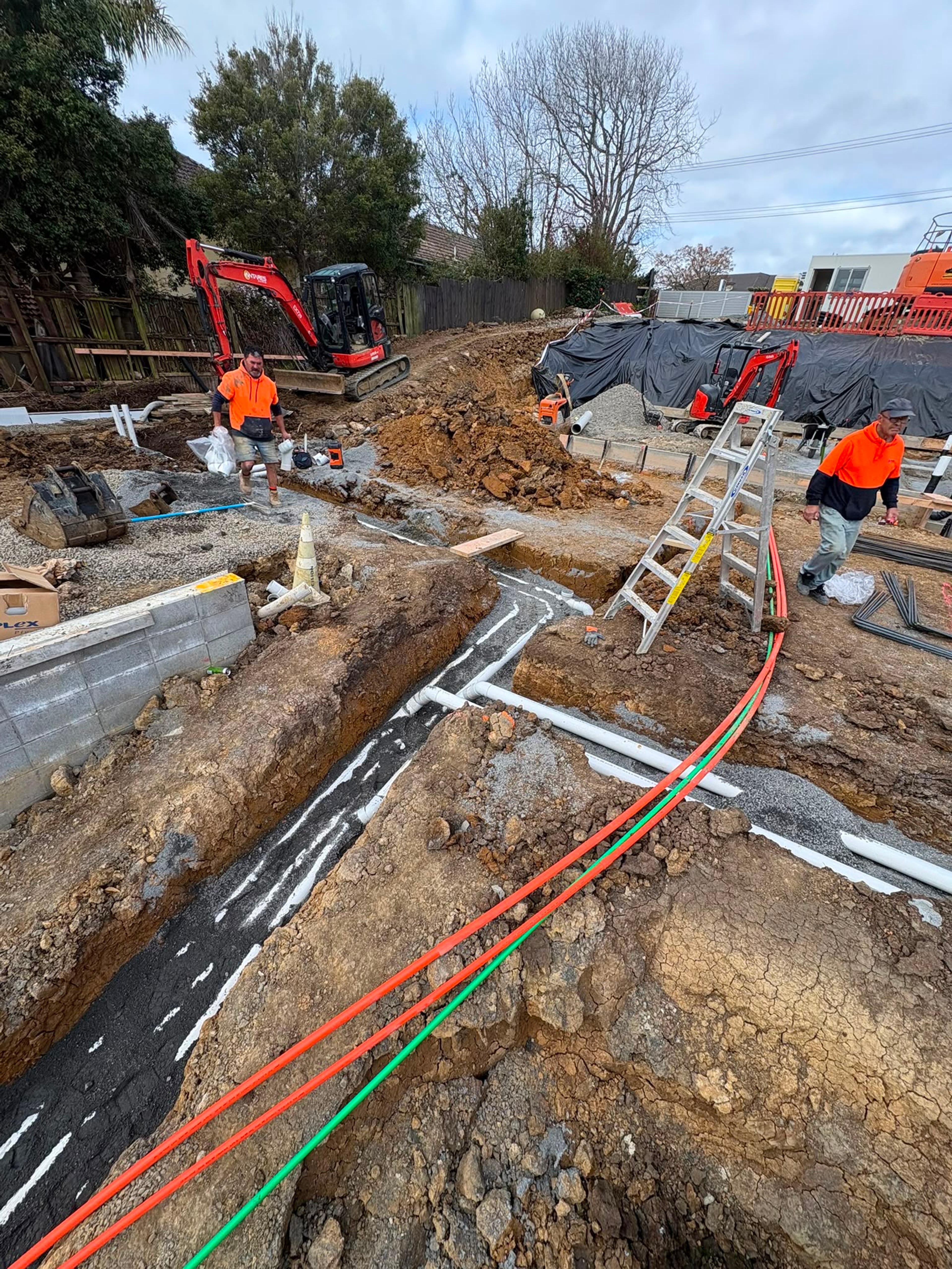Crew laying drainage alongside a new kerb with service conduits run in