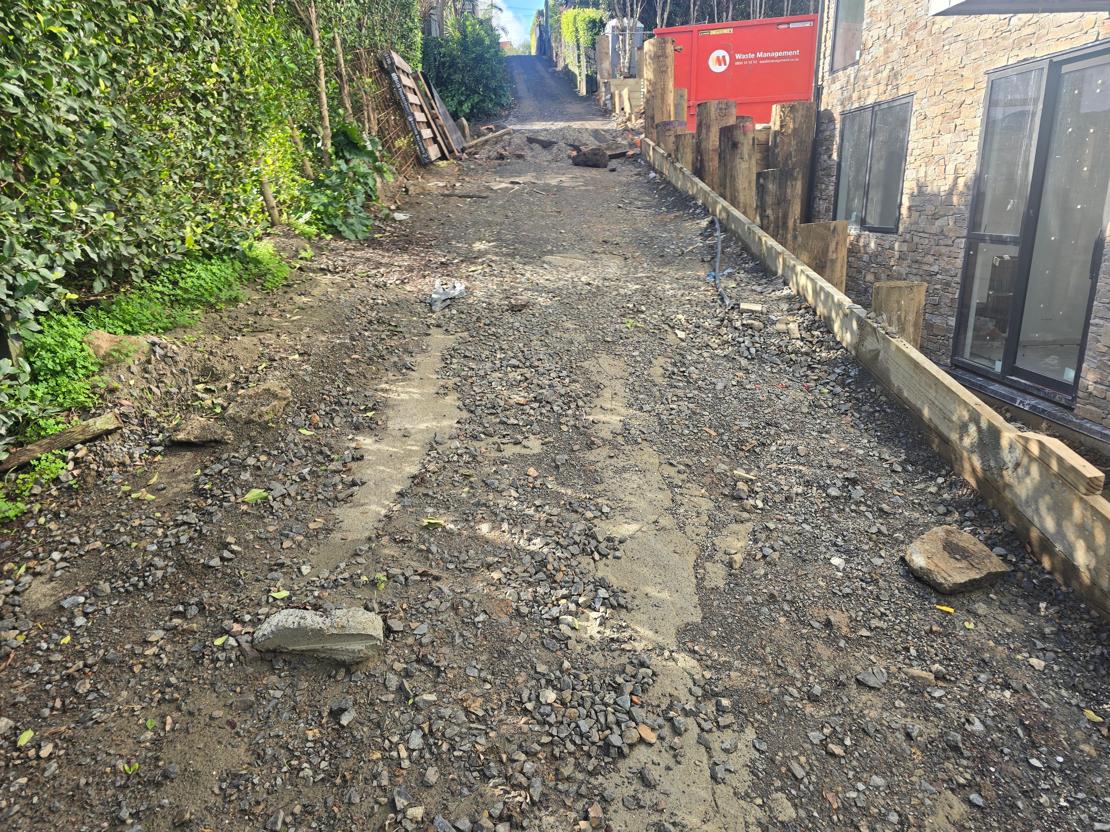 Driveway stripped back to basecourse between a hedge and a timber retaining wall