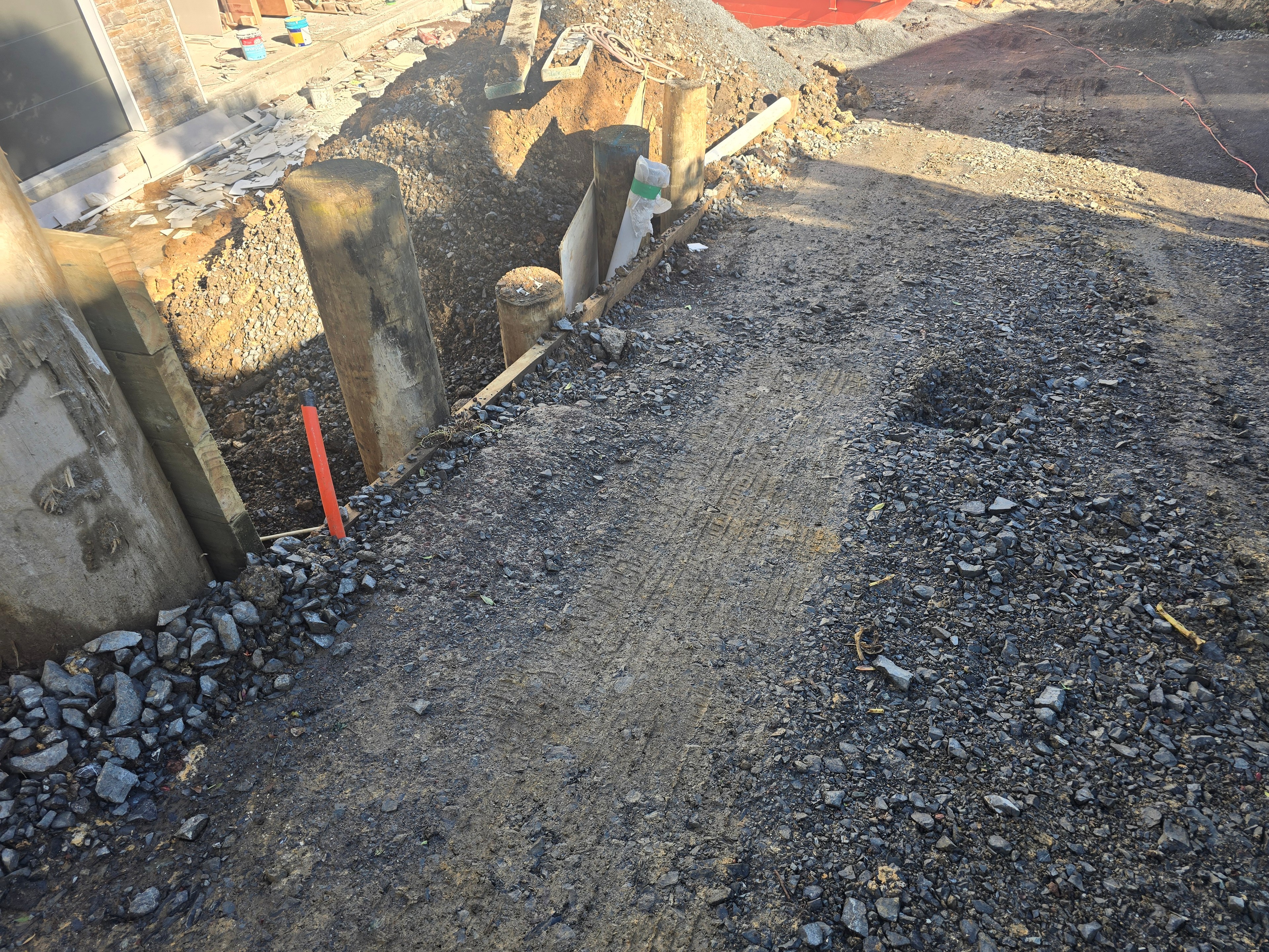 Timber retaining wall poles set in a trench with drainage metal backfilled behind them