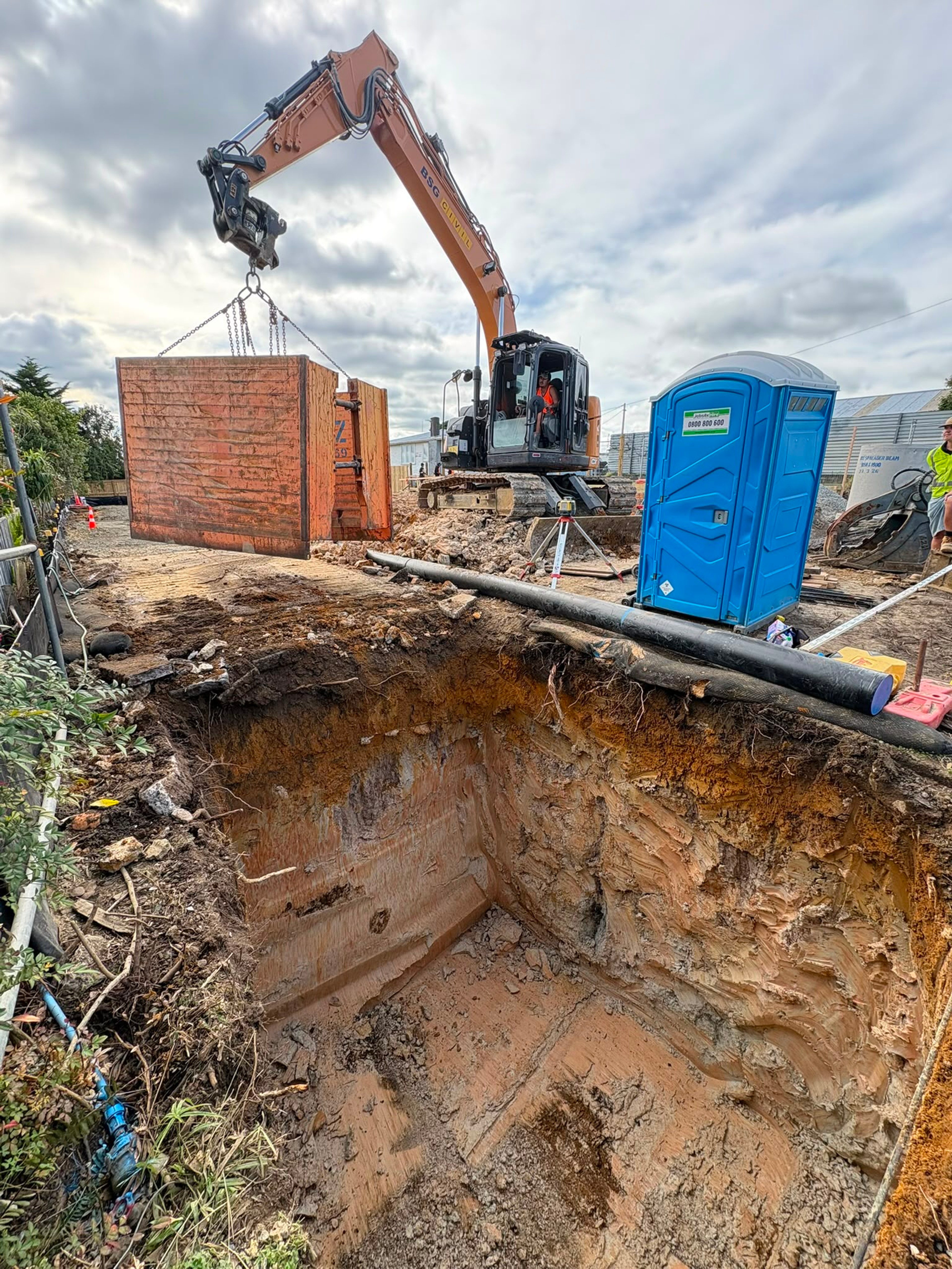Deep excavation beside a brick wall with the excavator craning material out