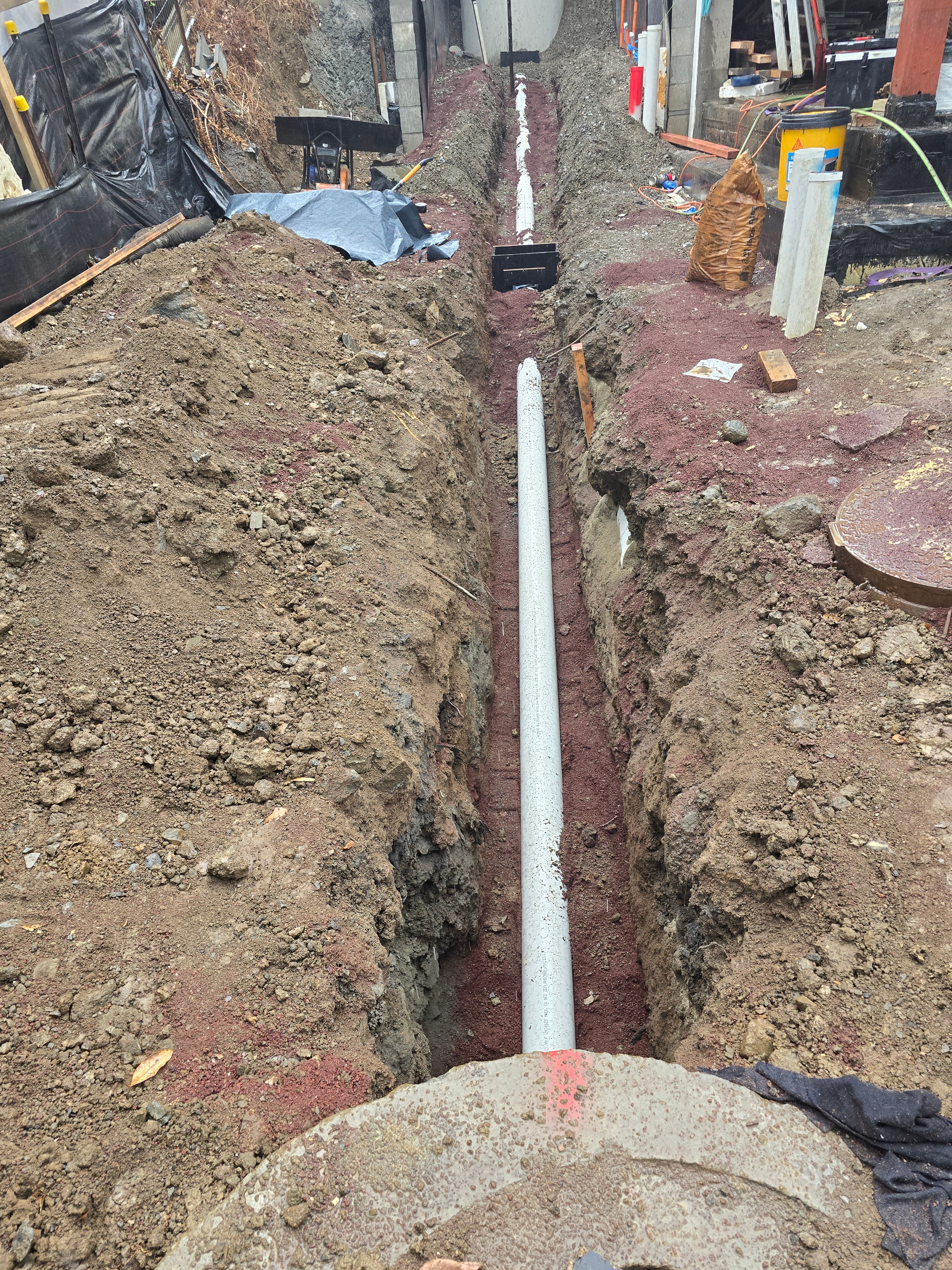 Stormwater pipe bedded on scoria in an open trench beside a new manhole